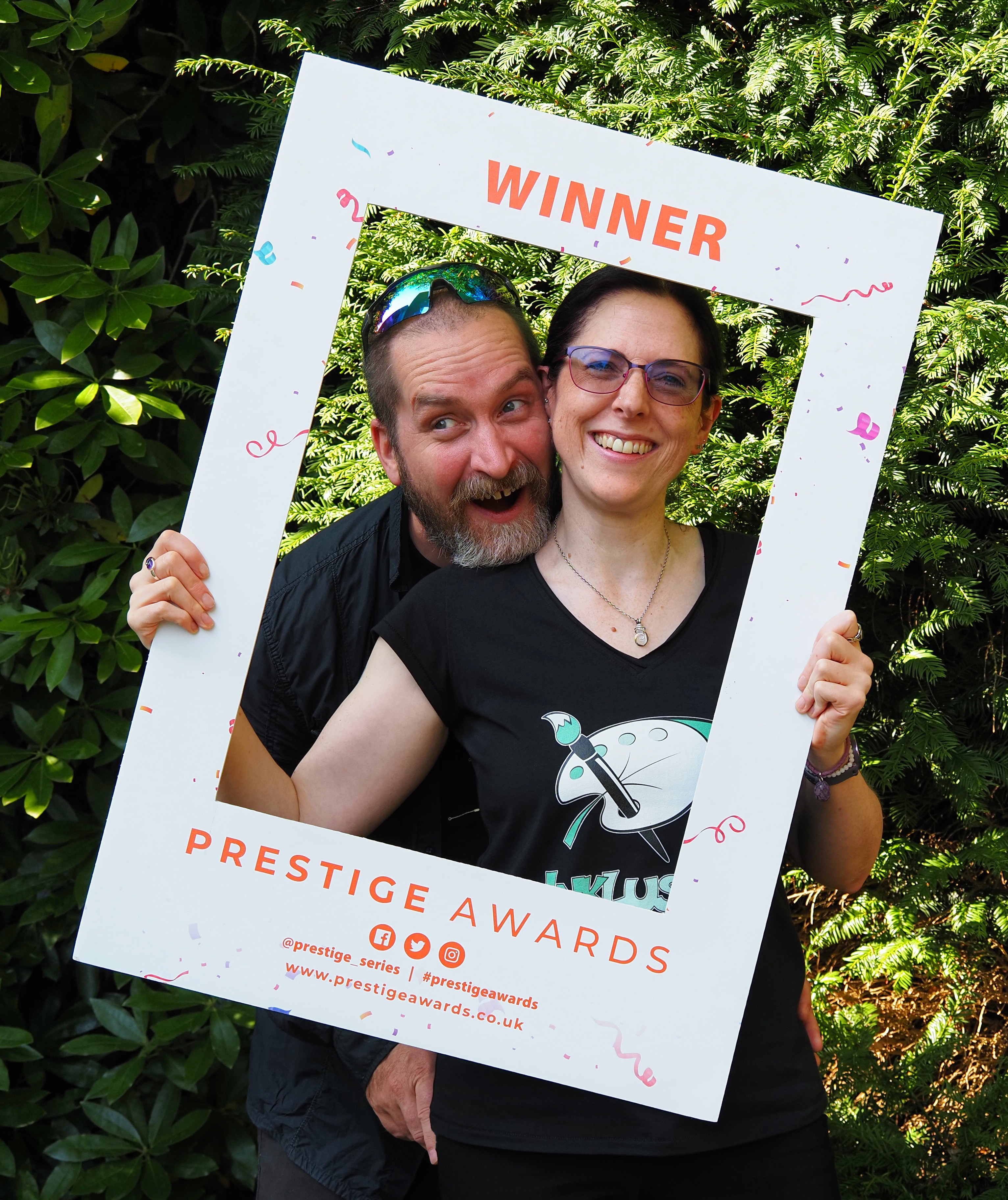 John and Vicky are smiling through a cardboard frame that reads: Winner, Prestige Awards